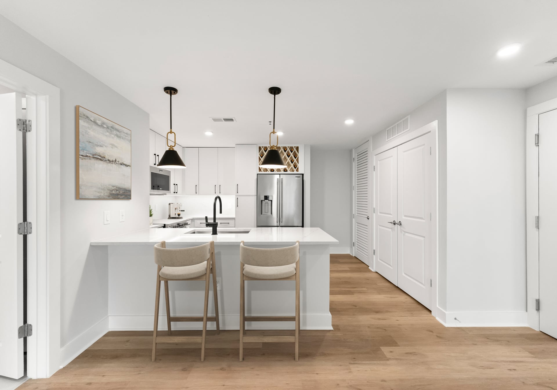 Modern white kitchen with island seating, pendant lights, and wood flooring in a bright open space.