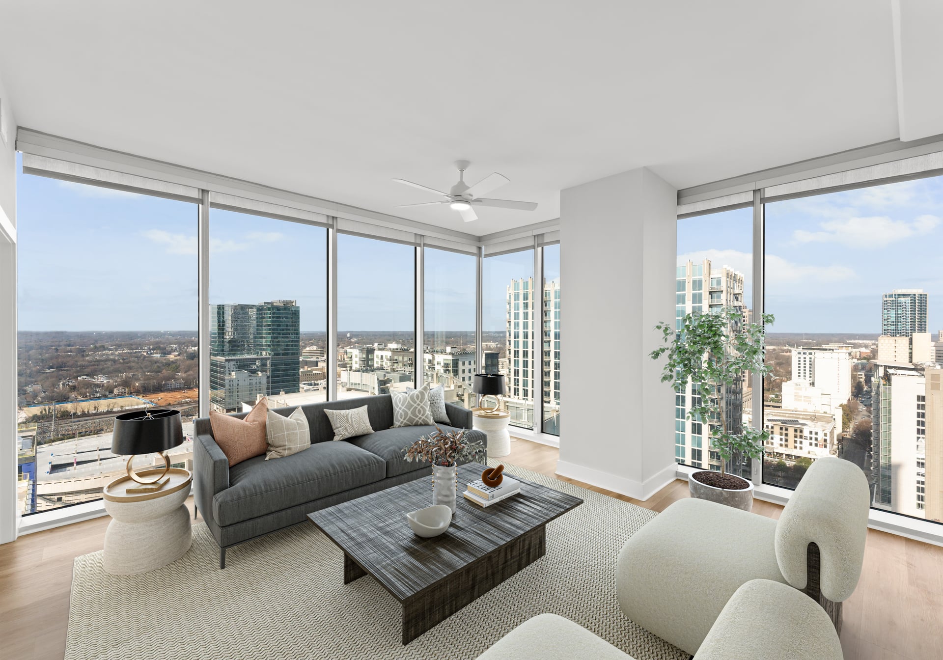 Modern living room with large windows offering a city skyline view, neutral furniture, and a potted plant.