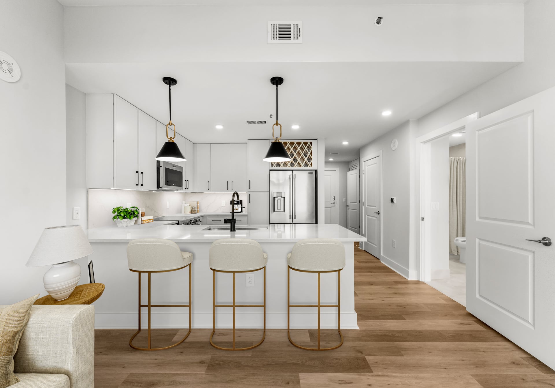 Modern kitchen with white cabinets, island with three stools, pendant lights, and stainless steel appliances.