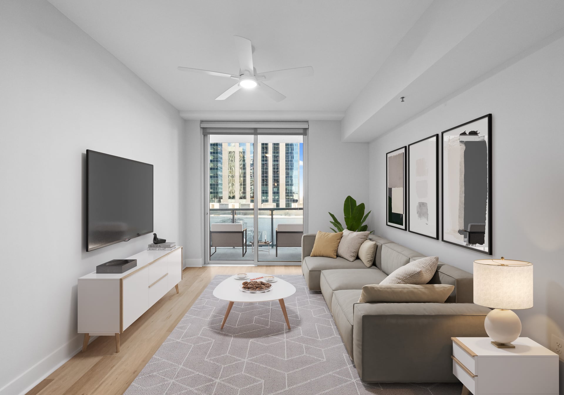 Modern living room with a sofa, coffee table, TV, wall art, lamp, and a balcony view of tall buildings.