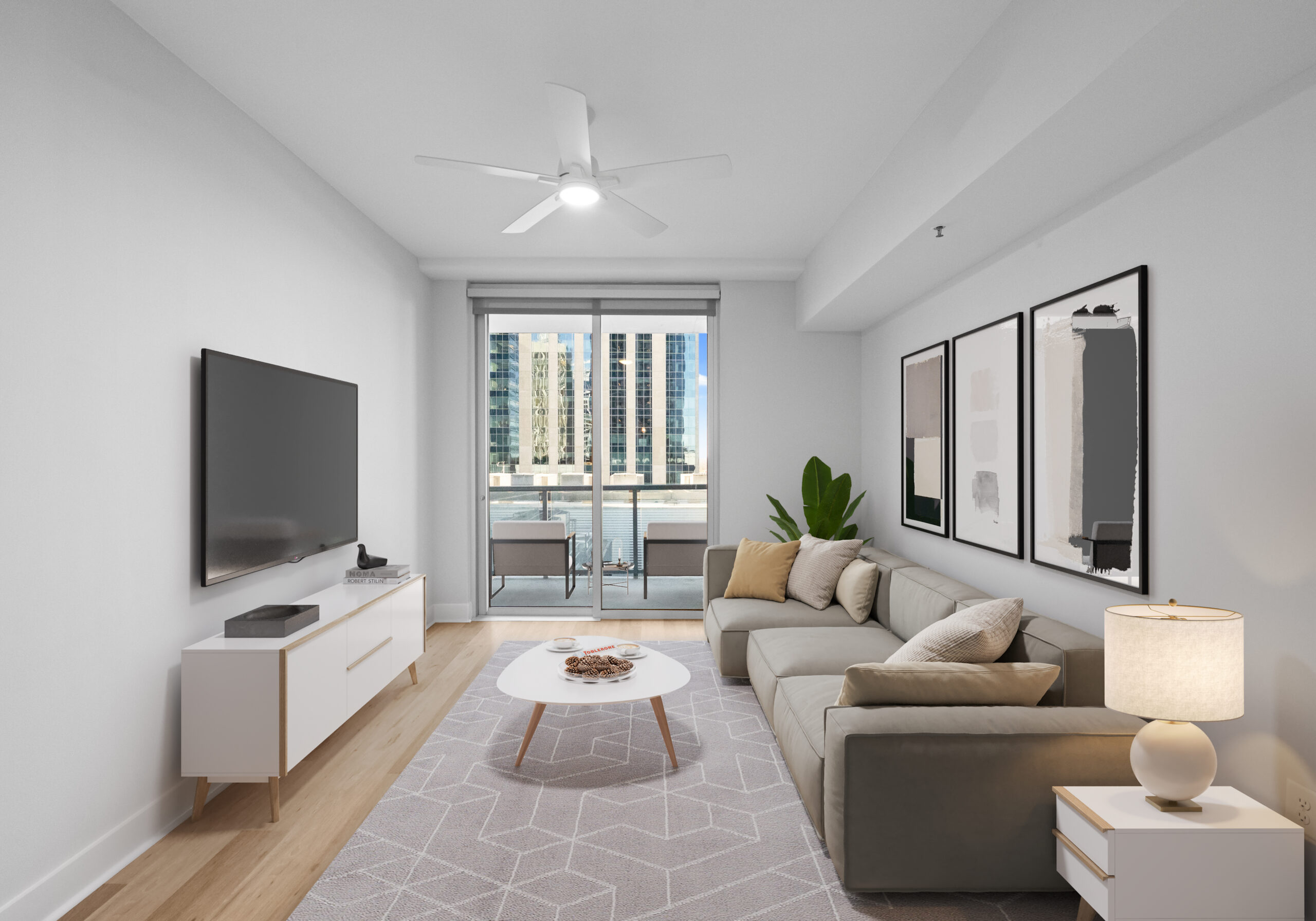 Modern living room with a gray sofa, wall art, TV, coffee table, lamp, and balcony view of city buildings through glass doors.