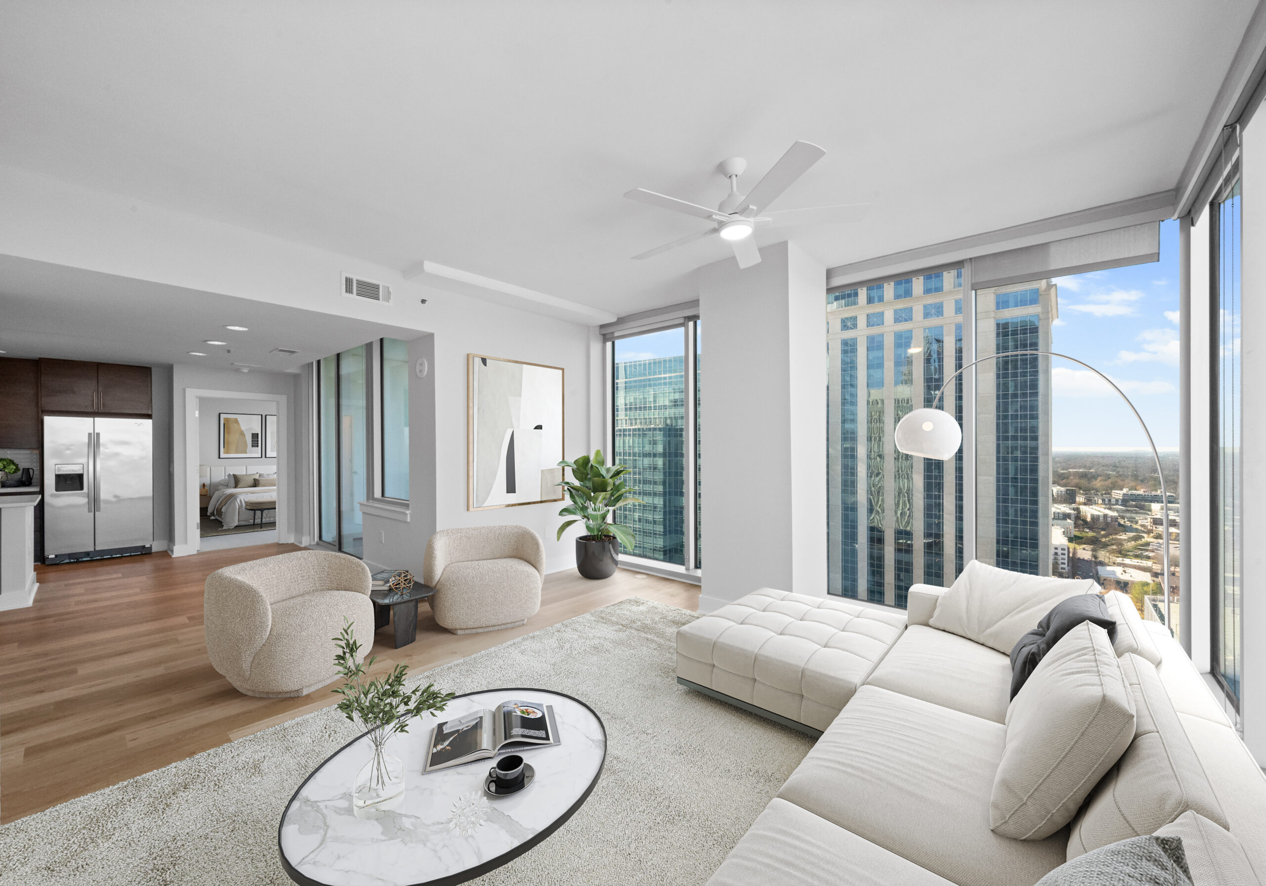 Modern living room with large windows, city views, white sofa, round chairs, and a kitchen in the background.