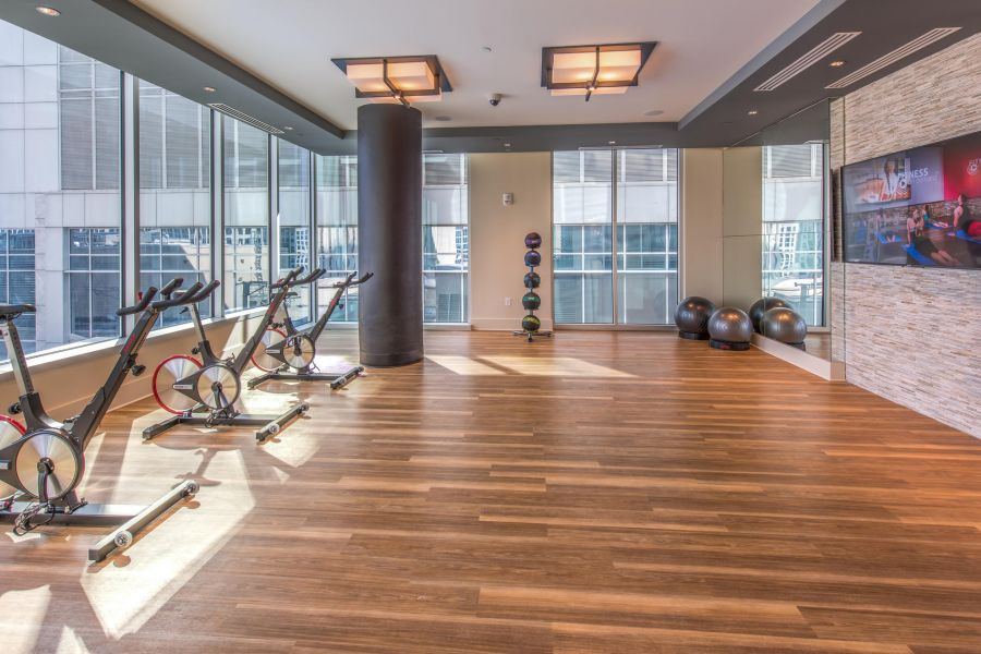 Modern gym room with three stationary bikes, exercise balls, kettlebells, and large windows letting in sunlight.
