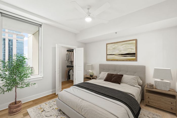 Modern bedroom with a bed, nightstands, large window, potted plant, and open closet door.