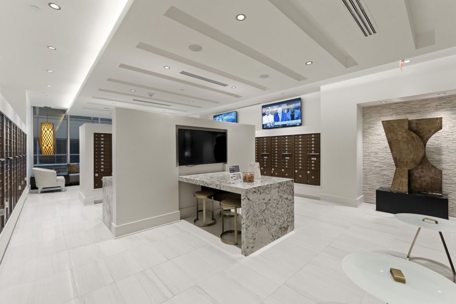 Modern lobby with marble counters, mailboxes, wall art, lounge chairs, and mounted TVs.
