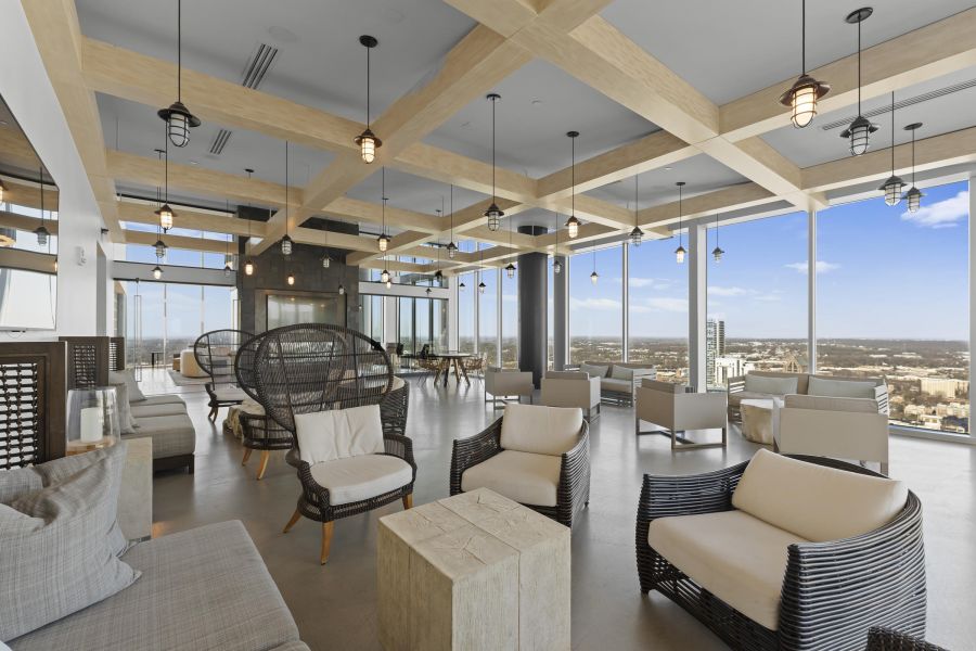 Modern lounge with wicker chairs, sofas, large windows, city views, and wooden ceiling beams.