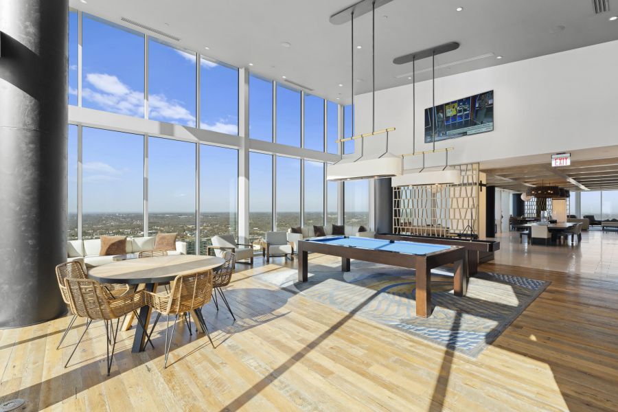 Modern lounge with pool table, round table and chairs, large windows, and city views under bright daylight.