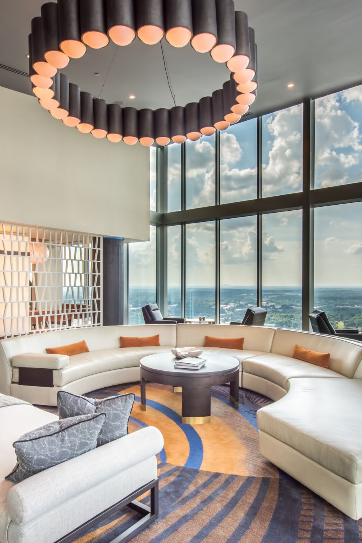 Spacious modern lounge with curved sofa, large windows, city view, wood floors, and a circular chandelier.