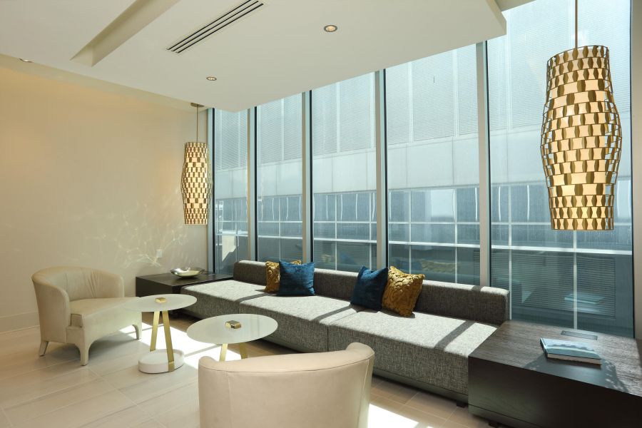 Modern lounge with large windows, a gray sofa, armchairs, round tables, and two woven pendant lights.