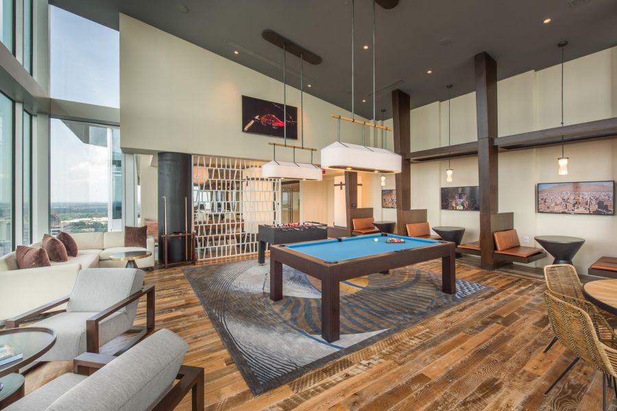 Modern lounge with pool table, foosball, large windows, seating areas, and city views in the background.